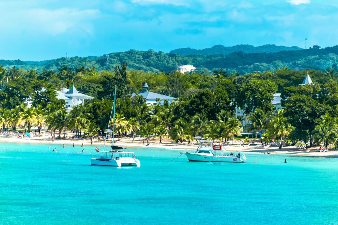 Catamarans off a palm-lined beach and waterfront buildings in Negril, Jamaica